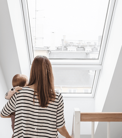 Femme portant un bébé dans ses bras en regardant la vilel de Saint-Etienne par sa fenêtre de toit