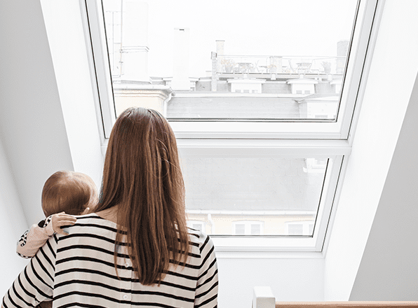 Femme portant un bébé dans ses bras en regardant la vilel de Saint-Etienne par sa fenêtre de toit